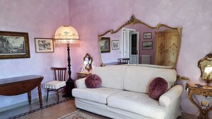 A room with a beige sofa, a wooden side table, a floor lamp, and a patterned rug. - VACATIONS IN THE HEART OF ROME COLOSSEUM (Roma)