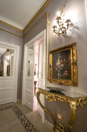 A hallway with a mirror, a chandelier, and a framed artwork on the wall. - VACATIONS IN THE HEART OF ROME COLOSSEUM (Roma)
