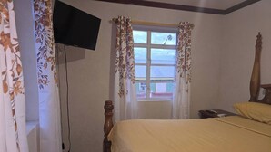 Ein Schlafzimmer mit einem hölzernen Bett, einem an der Wand befestigten Fernseher und einem Fenster mit blumigen Vorhängen.