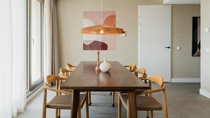 A modern dining area with a wooden table and chairs, a hanging light fixture, and a large abstract painting on the wall. - Apartment in Zeeheldenkwartier (The Hague)