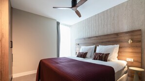 A modern hotel room with a large bed, a wooden headboard, a ceiling fan, and a small bedside table. - Apartment in Zeeheldenkwartier (The Hague)