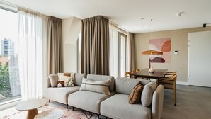 A modern living room with a sectional sofa, a dining table with chairs, and a large window with curtains. - Apartment in Zeeheldenkwartier (The Hague)