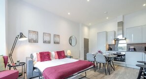 Une chambre d’hôtel moderne équipée d’un lit, de tables de chevet, d’un bureau et d’une kitchenette.
