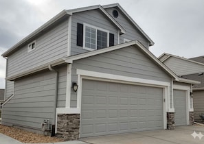 Une maison à deux étages avec un garage, des fondations en pierre et un toit en pente.
