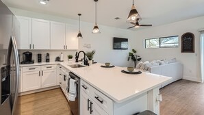 A modern kitchen with white cabinets, a large island, pendant lights, and a built-in oven.