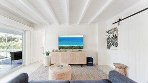 Una sala de estar moderna con un televisor grande, un sofá, una mesa de centro y vistas al océano.
