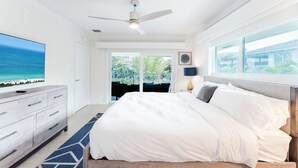Un dormitorio con cama, televisor, ventilador de techo y vista al exterior.