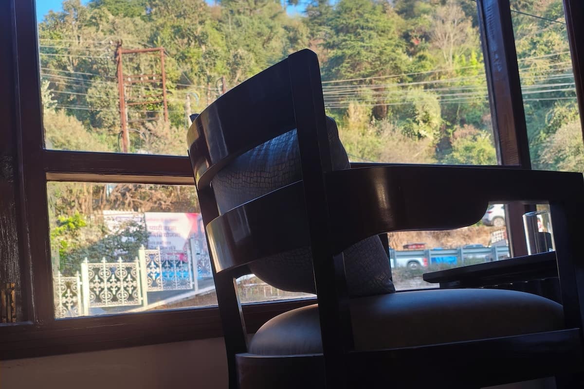 A wooden chair by a window with a view of a gate and trees.