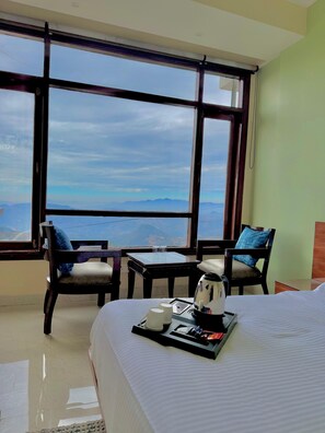 A hotel room with a large window offering a mountain view, a bed with a tray of breakfast items, and two chairs with blue cushions. - The waypointinn (Shimla)