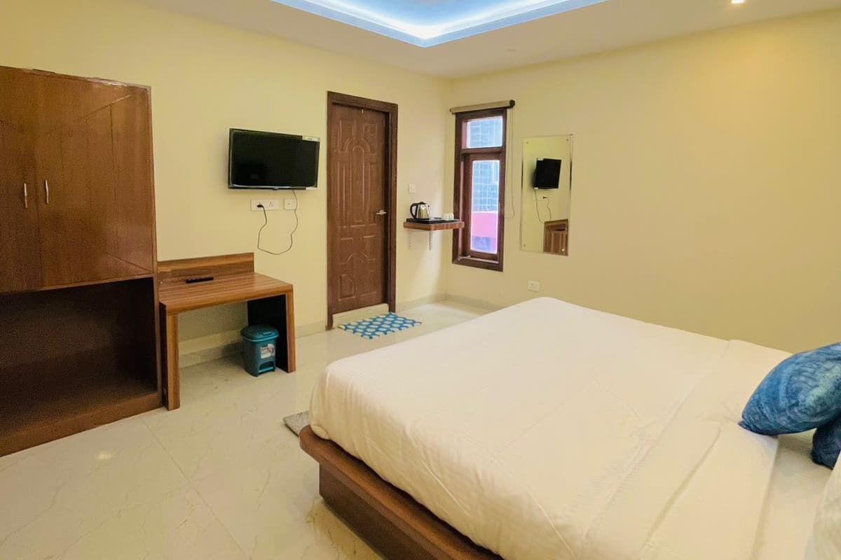 A bedroom with a bed, a wooden wardrobe, a desk, a television, and a window.