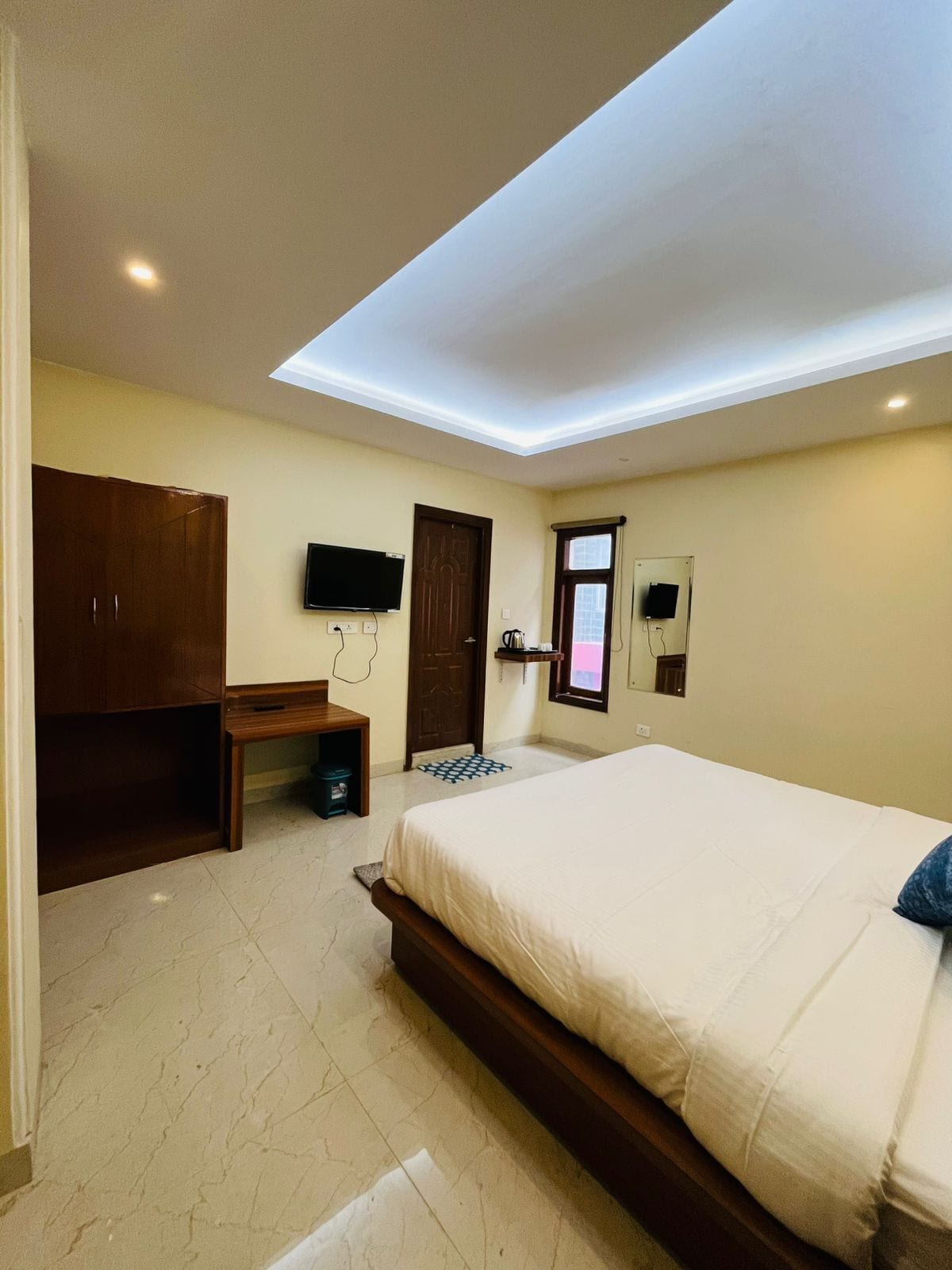 A bedroom with a bed, a desk, a wardrobe, a television, and a window.