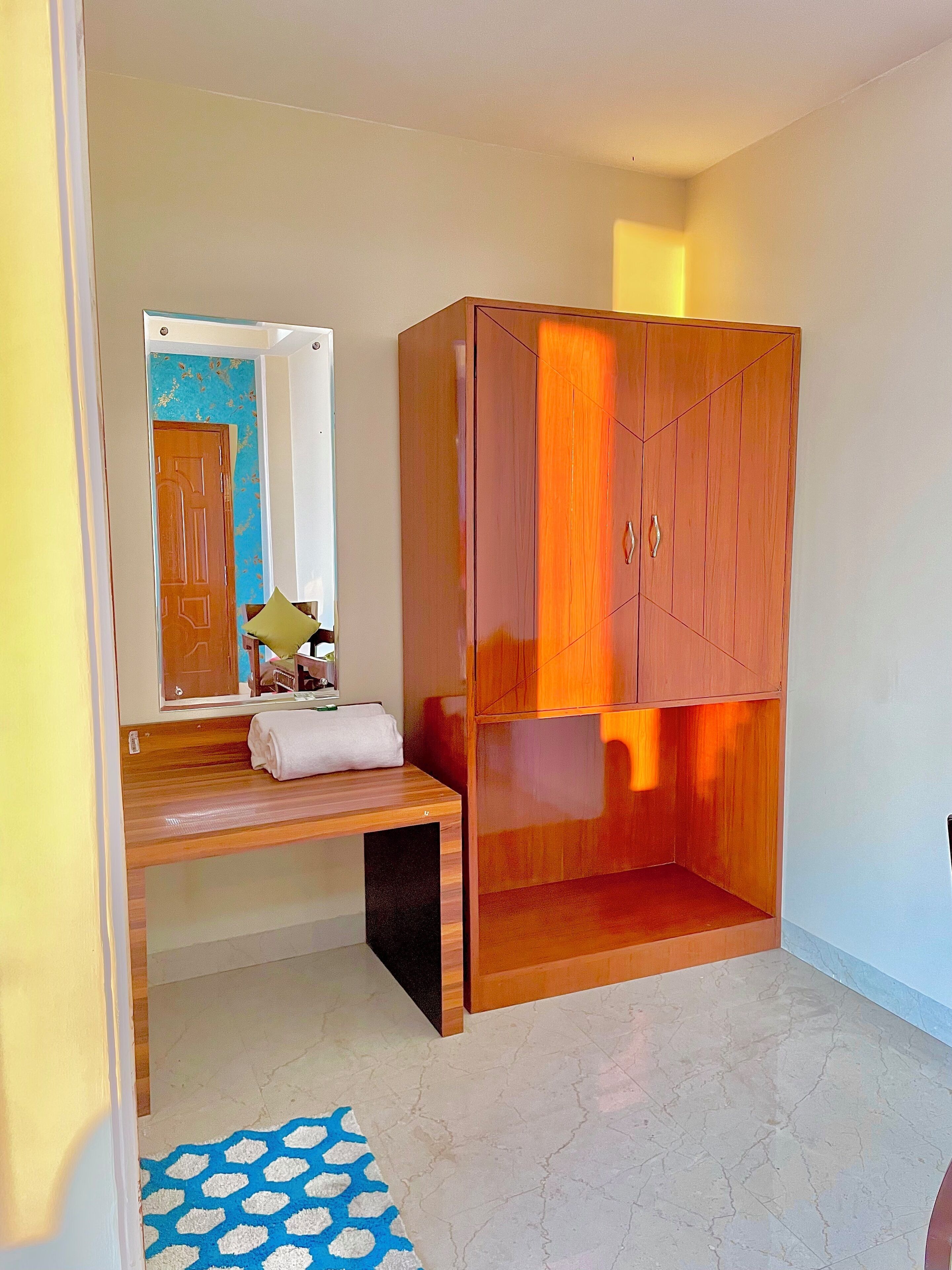 A room with a wooden wardrobe, a bench with a towel, and a patterned rug.