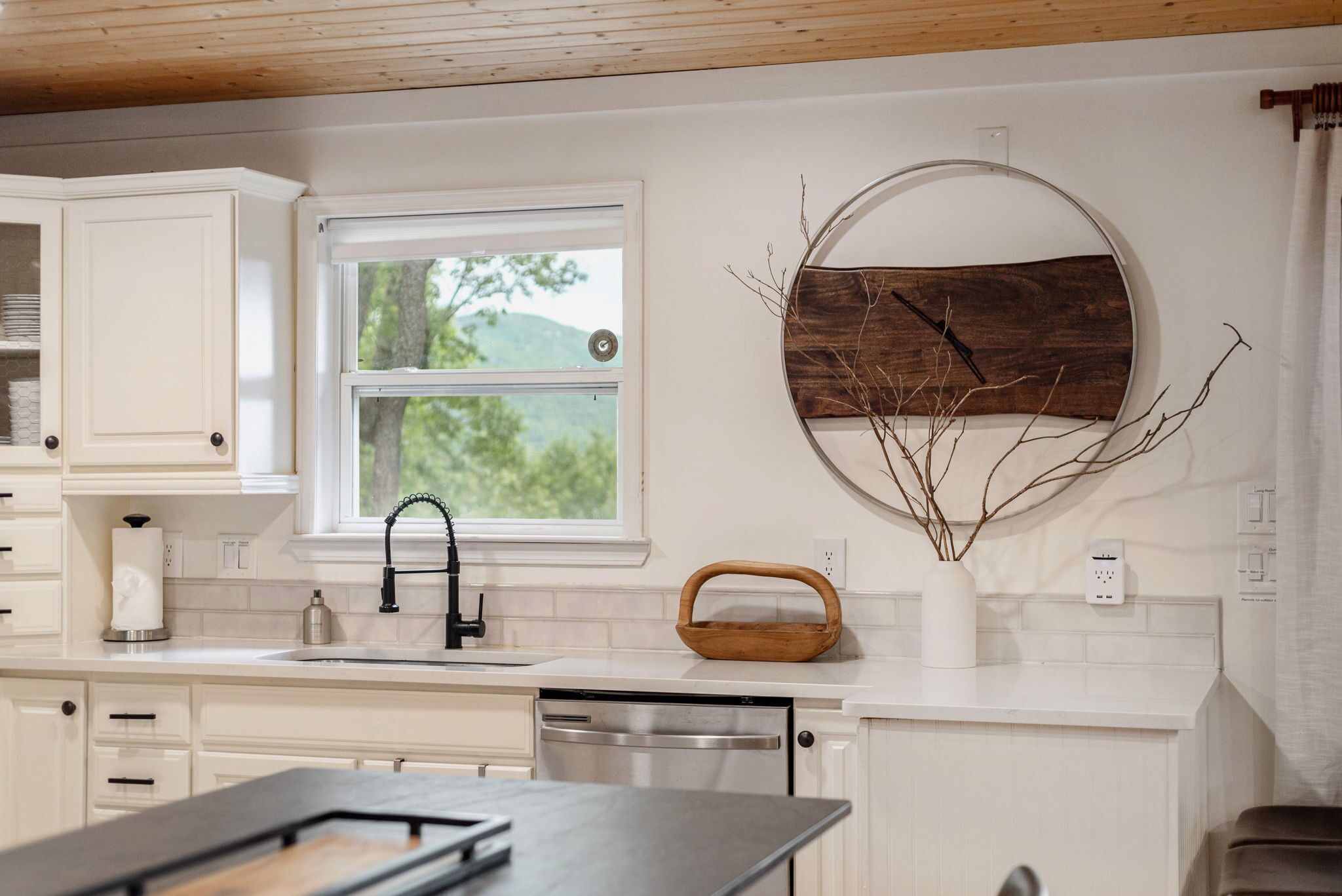 Eine moderne Küche mit weißen Schränken, einem großen Fenster, einer Holz-Wanduhren und einer schwarzen Arbeitsplatte.