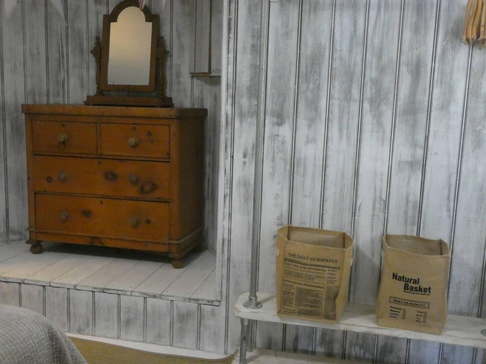 A wooden dresser with a mirror and drawers, a shelf with a newspaper and a bag labeled 'Natural Basket'.