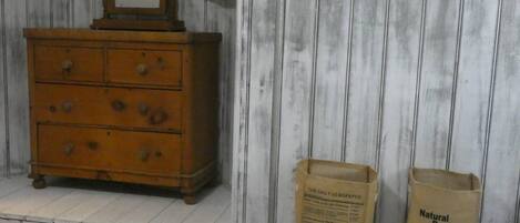A wooden dresser with a mirror and drawers, a shelf with a newspaper and a bag labeled 'Natural Basket'.