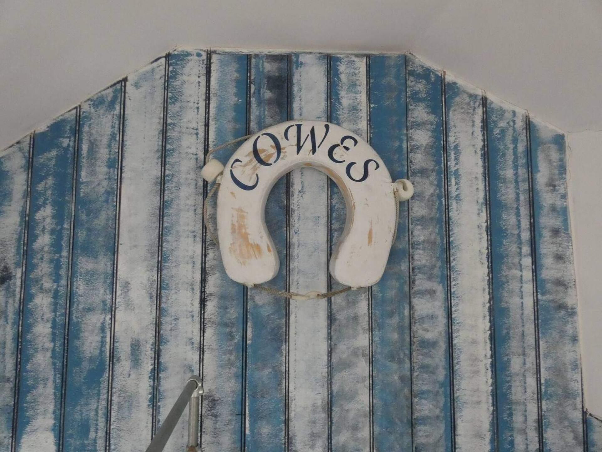 A rustic, blue-striped wall with a white, distressed sign that reads 'COWES.'