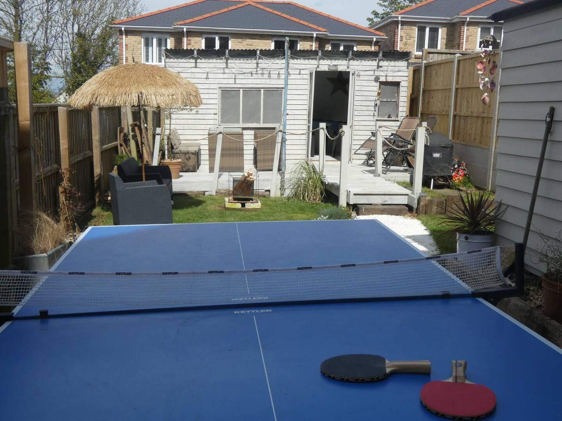 A backyard with a ping pong table, a thatched umbrella, and a house with a screened porch.