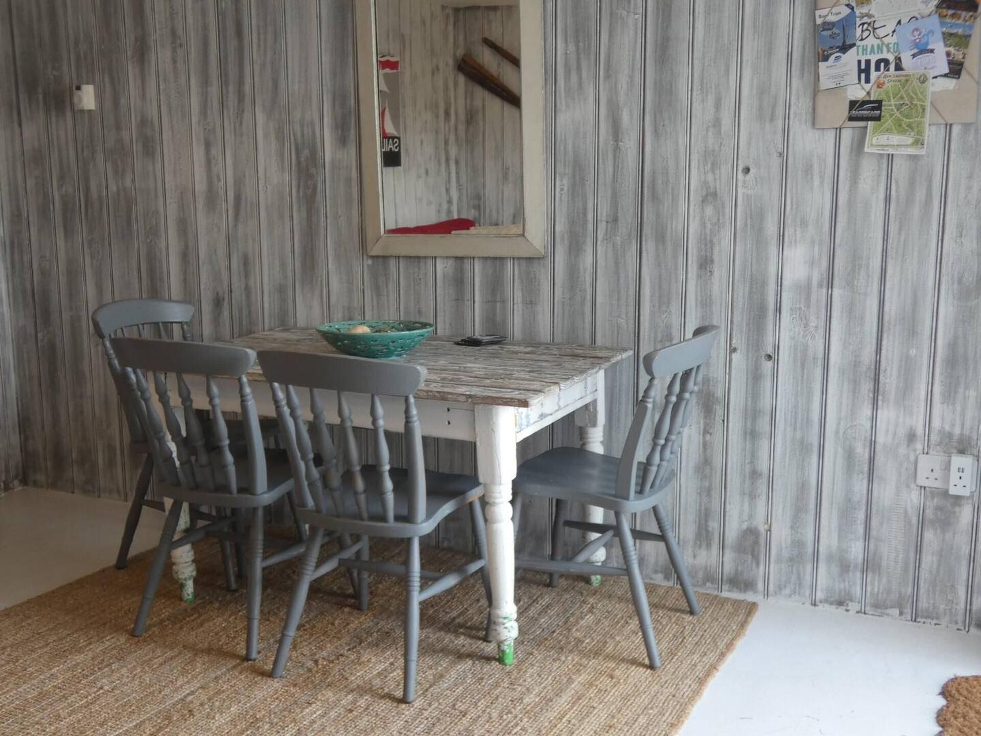 A dining area with a wooden wall, a table, four chairs, and a mirror.