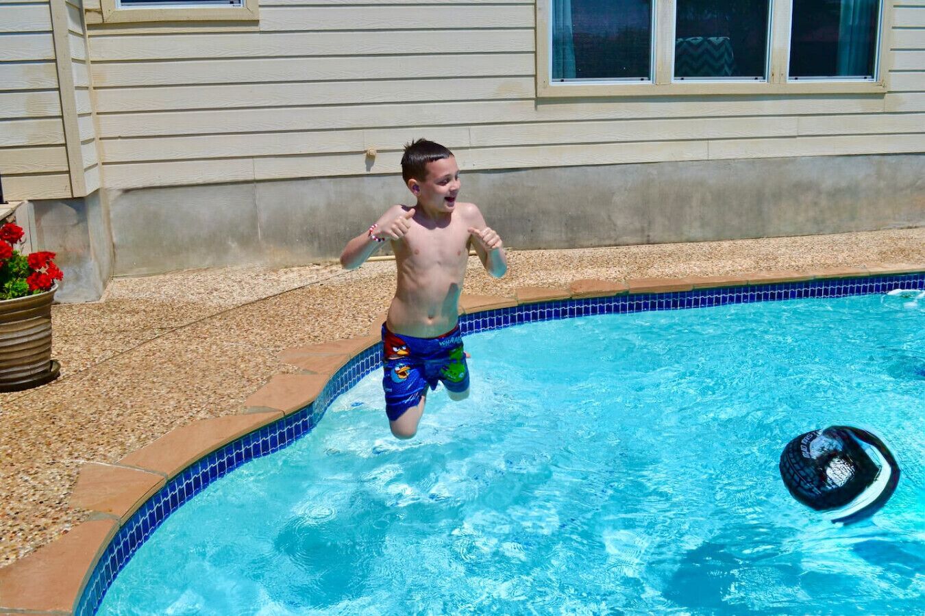 A child jumping into a swimming pool with a pool noodle.