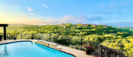 A swimming pool with a view of a lush garden and distant houses.