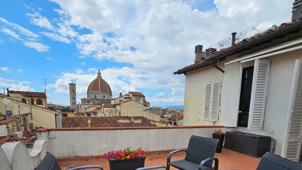 A rooftop terrace with outdoor furniture, a flower planter, and a view of a historic building with a dome.