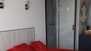 Une chambre à coucher moderne avec un grand lit, une cabine de douche en verre et une petite table de chevet.