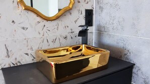 Une salle de bain avec un meuble-lavabo noir, un miroir encadré d’or et un lavabo de couleur or.