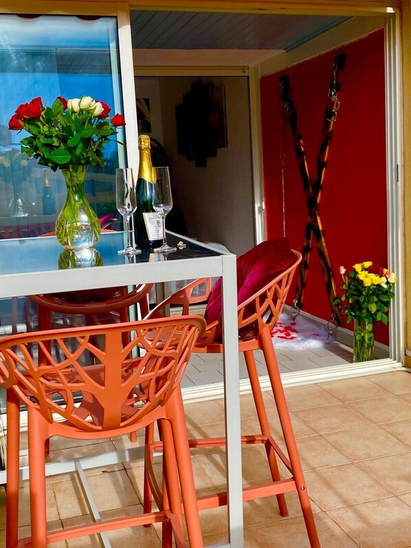En matplats med ett bord dukat för två personer, med en vas med blommor, en flaska champagne och två glas. Orangefärgade stolar är placerade runt bordet.