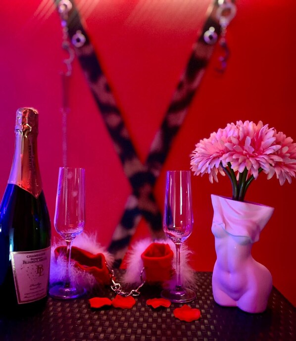 A table with a bottle, two glasses, a vase with flowers, and a feather.