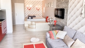 Ein moderner Wohnraum mit Sofa, Wand-Fernseher, einer Treppe zu einem Erkerbereich und einer Küchenzeile.