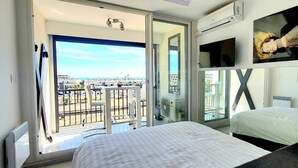 A hotel room with a balcony, a bed, a TV, and a large window. - Naturiste Cap d'Agde Héliopolis F 72 (Agde)