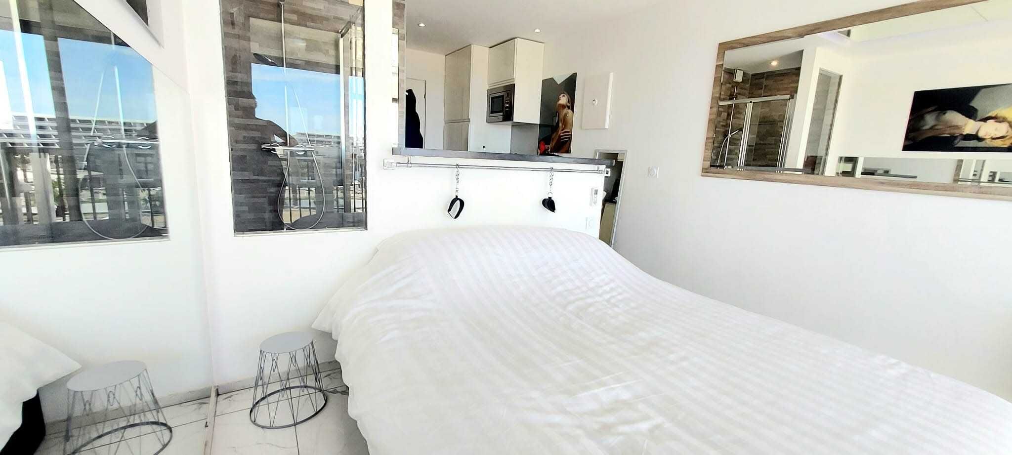 A modern bedroom with a large bed, a small round table, a mirror, and a view of the city through a window.