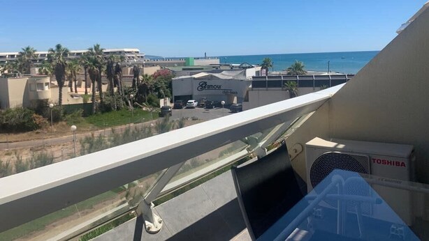 A view from a balcony overlooking a beach with a clear sky. There is a large truck labeled 'Glamour' and a 'TOSHIBA' air conditioning unit visible.