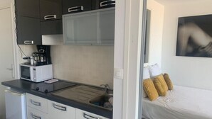 A compact kitchen with a microwave, coffee maker, and a sink. There is a bed with a white mattress and two pillows.