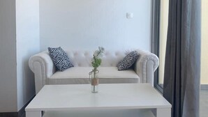 A modern living room with a white sofa, two black and white patterned pillows, a white coffee table, and a decorative piece on the wall.