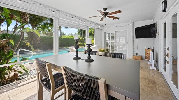 A spacious indoor area with a large table and chairs, a ceiling fan, and a view of a swimming pool outside. - Stylish 2-Bedroom, 2-Bathroom Home with Pool – Just Steps from the Beach! (Jupiter)