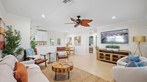 A modern living room with a sofa, coffee table, and chairs. There is a dining area with a table and chairs, and a kitchen in the background. - Stylish 2-Bedroom, 2-Bathroom Home with Pool – Just Steps from the Beach! (Jupiter)