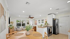 A modern kitchen with white cabinets, a black refrigerator, and a dining area with a wooden table and woven placemats. - Stylish 2-Bedroom, 2-Bathroom Home with Pool – Just Steps from the Beach! (Jupiter)