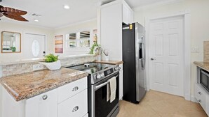 A modern kitchen with white cabinetry, granite countertops, a stainless steel refrigerator, and a built-in oven. - Stylish 2-Bedroom, 2-Bathroom Home with Pool – Just Steps from the Beach! (Jupiter)