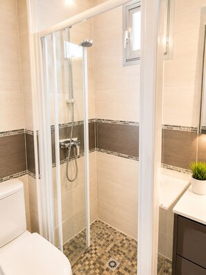 A bathroom with a glass-enclosed shower, a toilet, a sink with a mirror, and a potted plant.