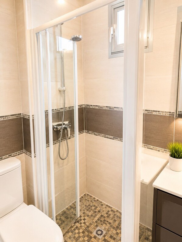 A bathroom with a glass-enclosed shower, a toilet, a sink with a mirror, and a potted plant.