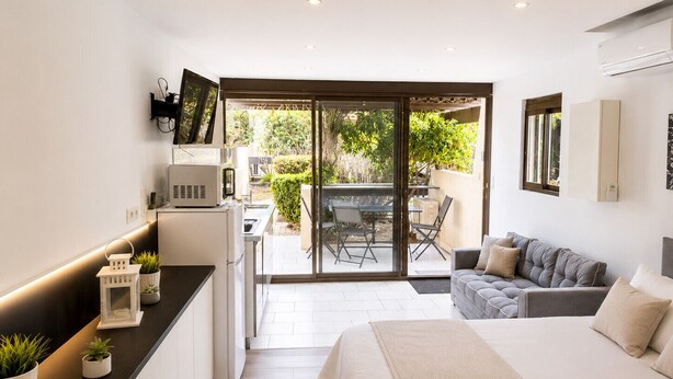 Une chambre moderne comprenant un lit, un canapé, un coin cuisine et une porte-fenêtre coulissante donnant sur une terrasse extérieure.