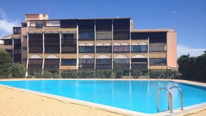 Une piscine dotée d’une terrasse carrelée, entourée d’un immeuble à plusieurs étages avec des balcons.