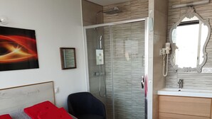 Ein Hotelzimmer mit Bett, Stuhl, Duschbereich und einem Badezimmer inklusive Spiegel und Waschbecken.