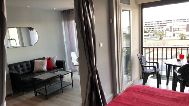 A hotel room with a bed, a sofa, a coffee table, and a balcony with chairs and a table. - Naturiste Cap d'Agde Héliopolis F 31 (Agde)