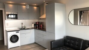 A compact kitchen with a washing machine, a coffee maker, and a microwave. There is a black leather sofa and a small table in the living area. - Naturiste Cap d'Agde Héliopolis F 31 (Agde)