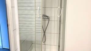 Une douche fermée par des parois en verre, dotée d’un pommeau de douche à main et d’un robinet mural fixe.