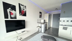 Un salon moderne doté d’un téléviseur à écran plat, d’un petit coin cuisine avec un four à micro-ondes et d’un coin repas avec un tabouret de bar.