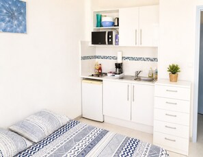A compact kitchen with white cabinets, a microwave, a coffee maker, and a sink. There is a small potted plant on the counter. - Naturiste Cap d'Agde Héliopolis L 24 (Agde)