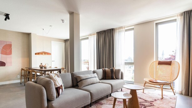 A modern living room with a sectional sofa, a dining table, and a wicker chair. - Spacious Apartment in Den Haag With View (The Hague)